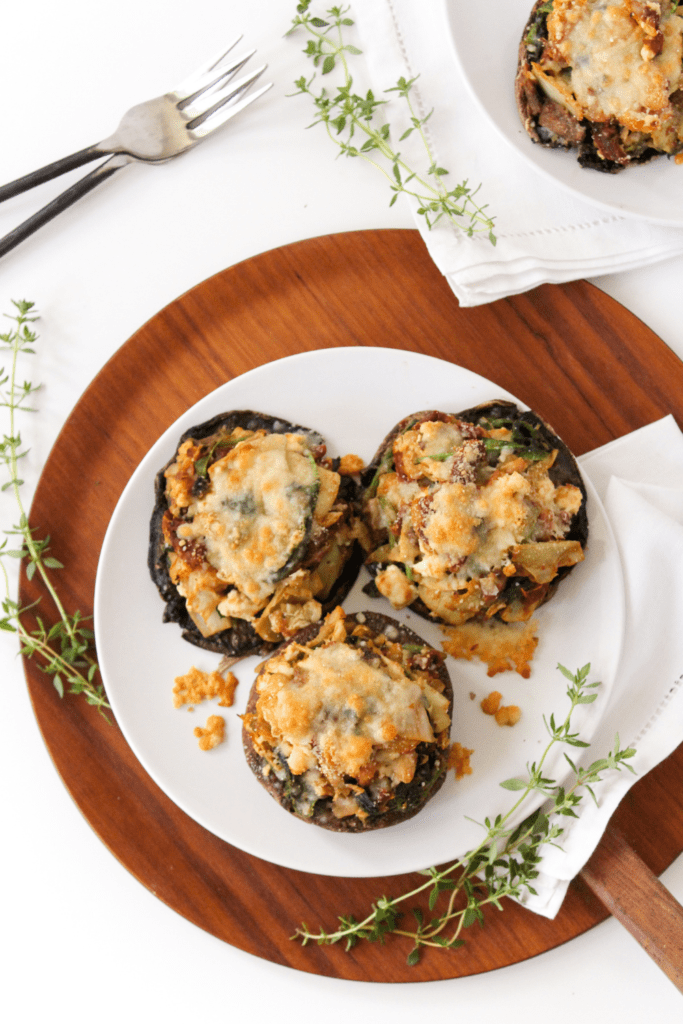 spinach artichoke stuffed mushrooms on a white plate with herbs