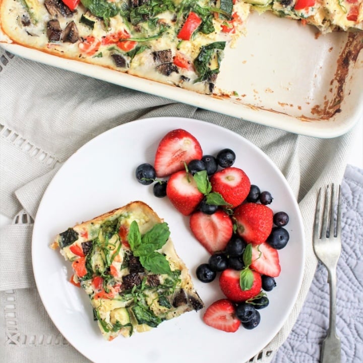 smoked salmon and veggie egg casserole in a dish with a slice cut out, served with fruit