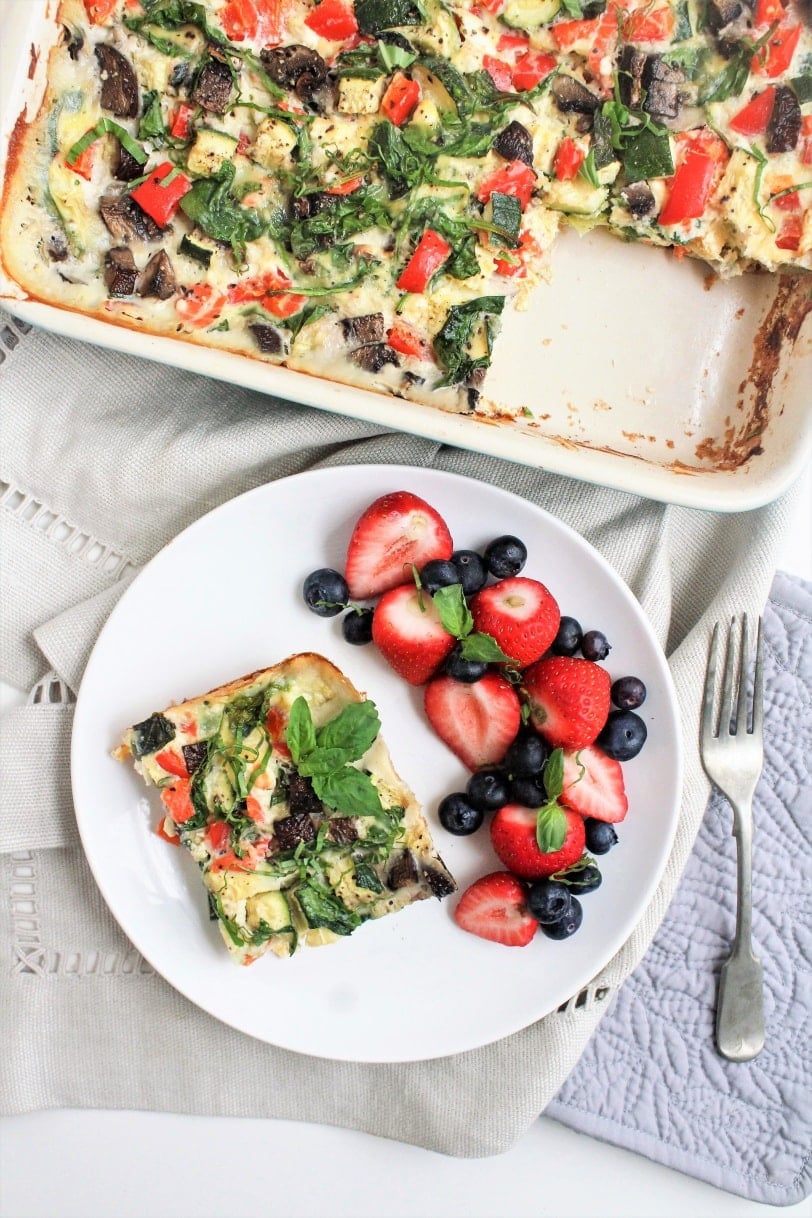 smoked salmon and veggie egg casserole in a dish with a slice cut out, served with fruit