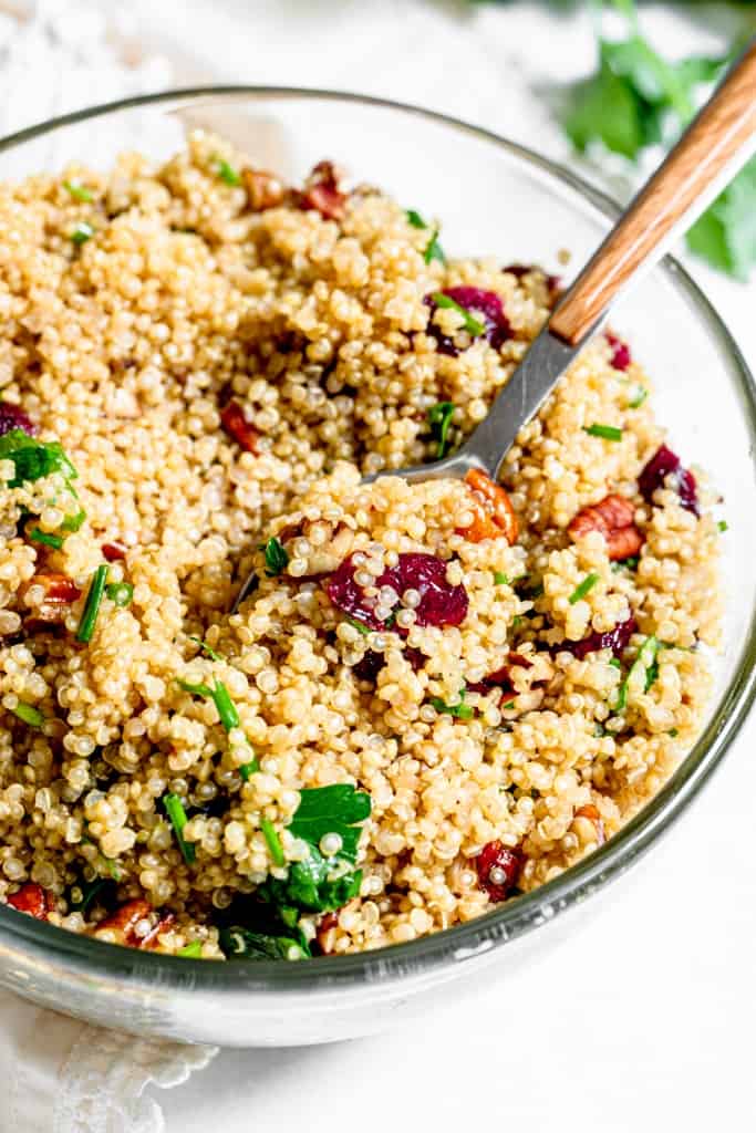 vegan quinoa salad with cranberries and pecans in a bowl with a wooden spoon