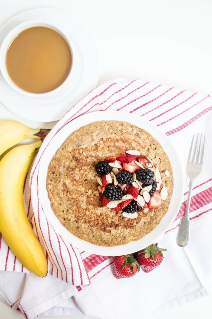 protein pancakes with banana, topped with berries and sliced almonds with a cup of coffee beside it