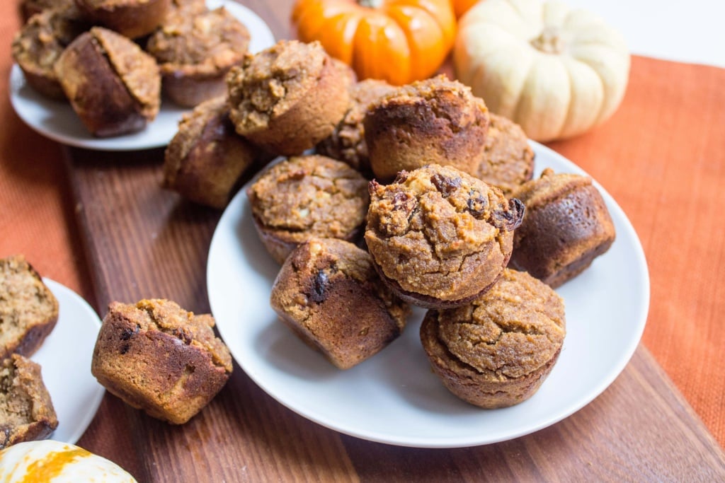 pumpkin muffins on a plate with mini pumpkins behind them