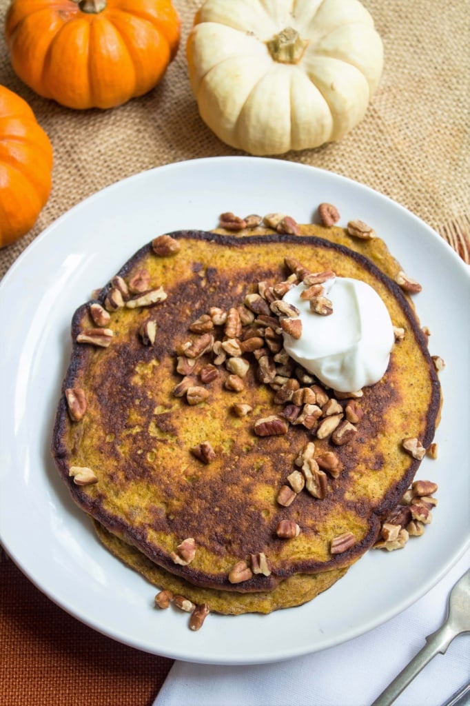 pumpkin pancakes with pecans and yogurt on top with mini pumpkins next to the plate