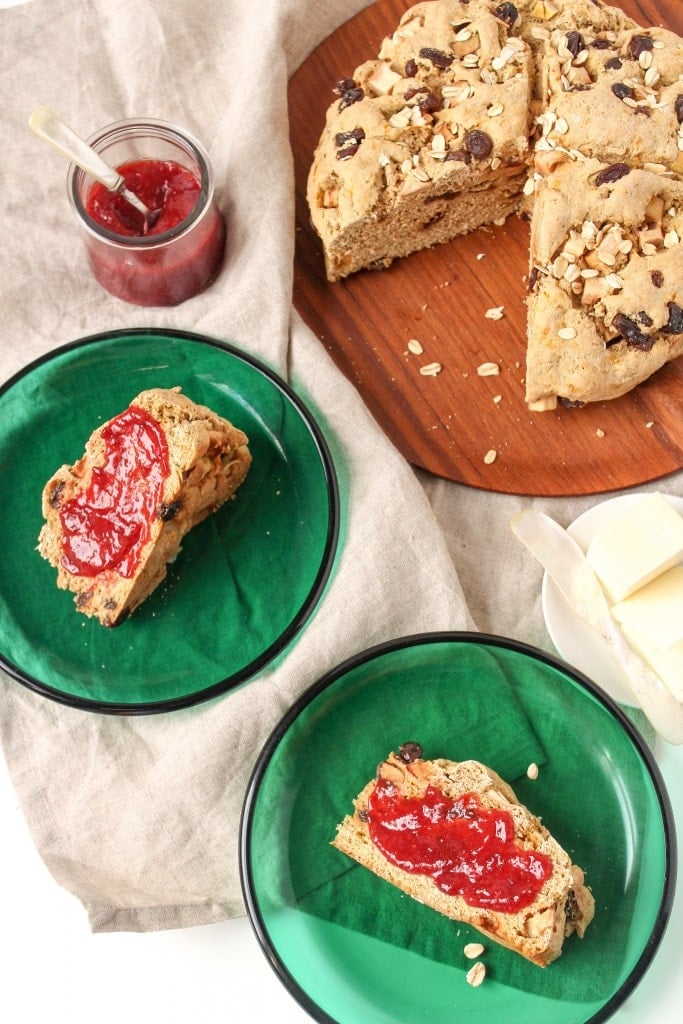 vegan soda bread on a wooden platter with a jam jar and bread slices on green glass plates