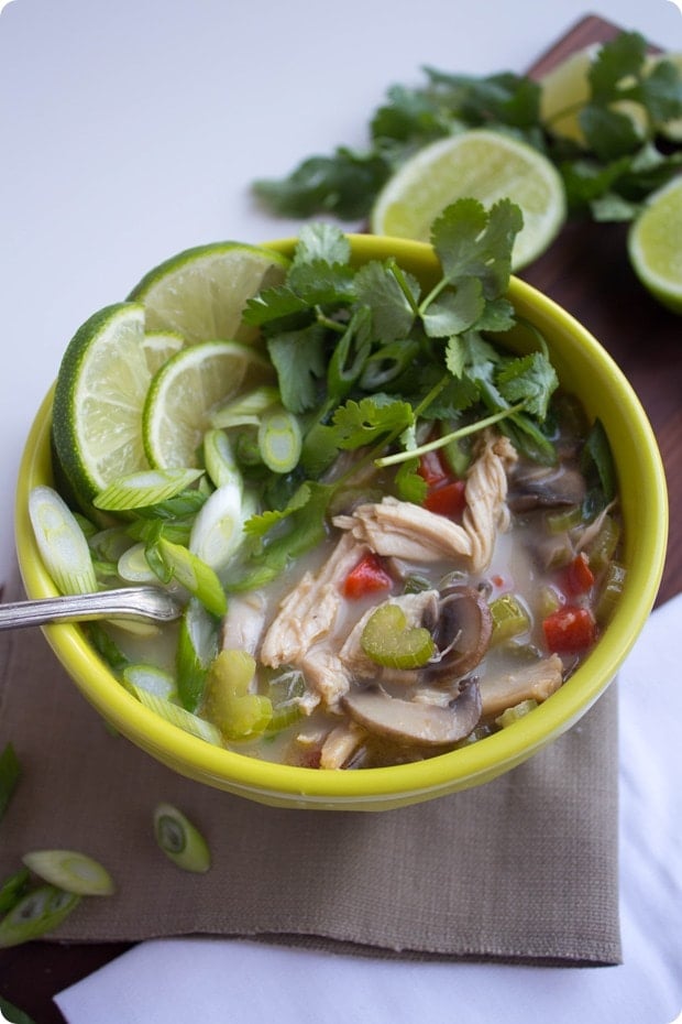 thai coconut chicken soup in a bowl with limes and herbs