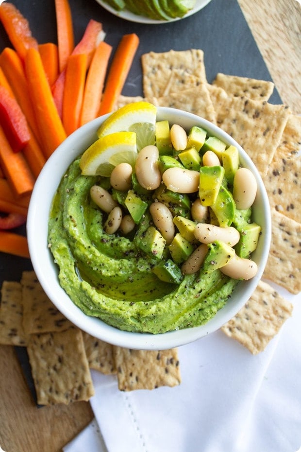 lemon avocado white bean hummus in a small white bowl with carrots and crackers beside it