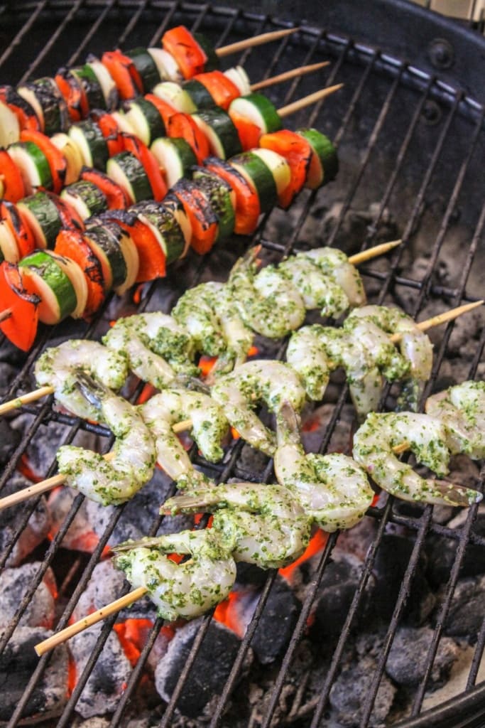 raw shrimp skewers on a grill with vegetable skewers