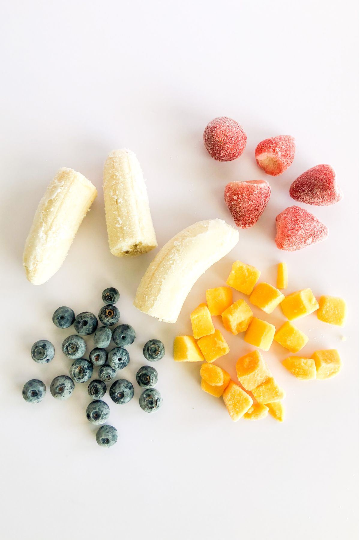 frozen banana, blueberries, diced mango, and strawberries on a white countertop