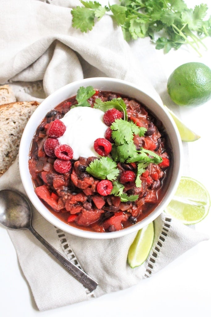 raspberry black bean chili in a bowl with lime slices and crusty bread surrounding it