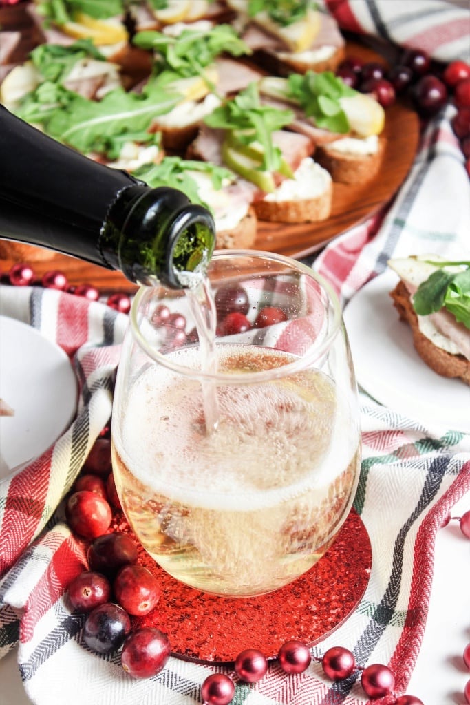 sparkling wine being poured into a glass with goat cheese crostini in the background