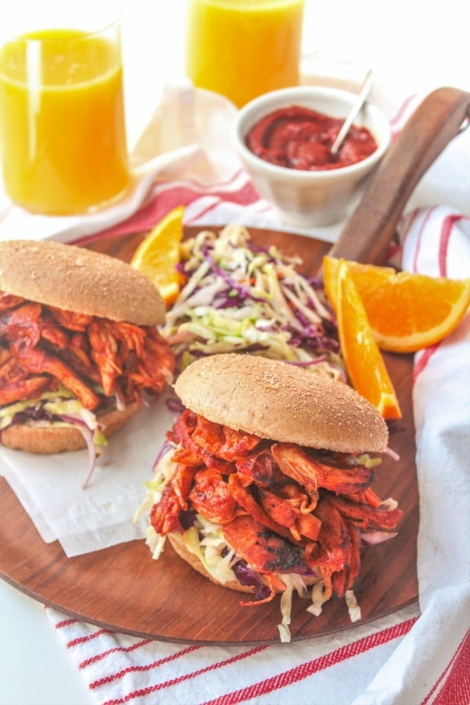 BBQ Chicken Sandwiches on a wooden platter with orange slices and glasses of orange juice