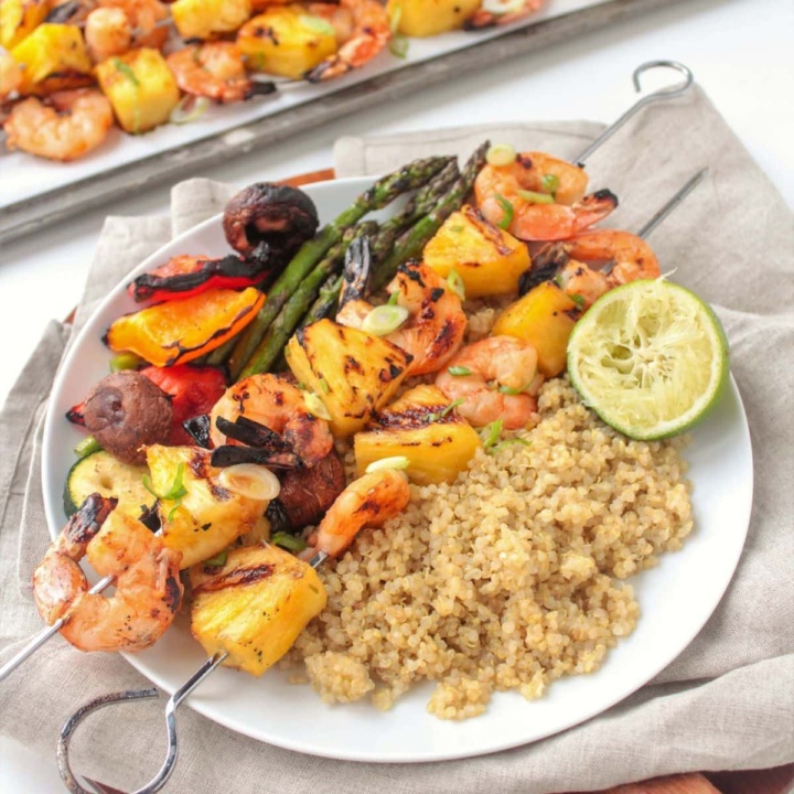 grilled shrimp and pineapple kabobs on a white plate with grilled vegetables and coconut quinoa