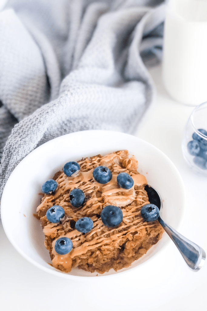 baked oatmeal with banana, blueberries, and peanut butter drizzle with a glass of milk in the background