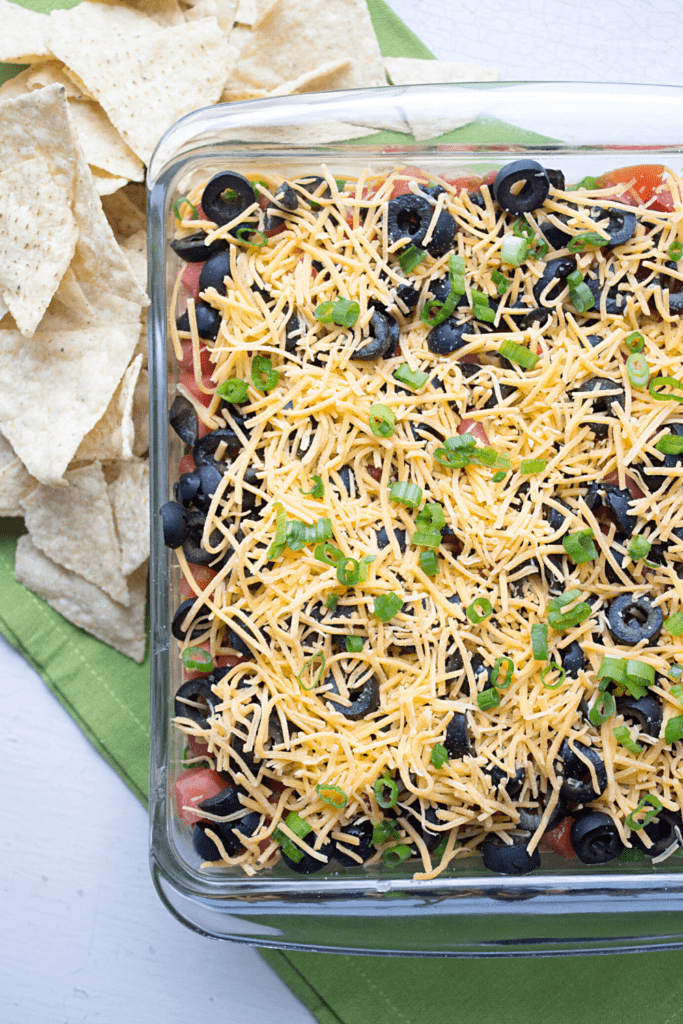 healthy 7 layer dip in a glass dish with tortilla chips