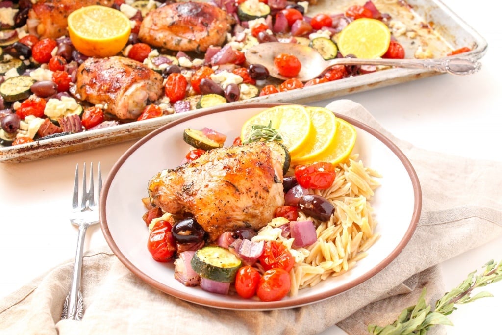 Mediterranean chicken thighs on a sheet pan with cherry tomatoes, zucchini, red onion, and orzo