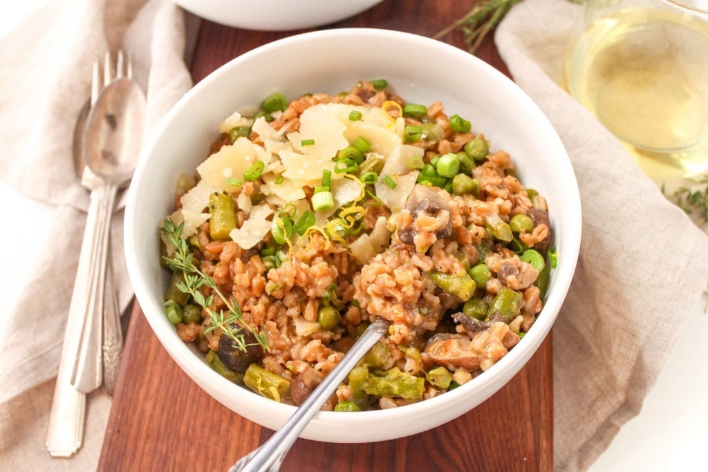 farro risotto in a white bowl on a wooden platter with a glass of white wine in the background