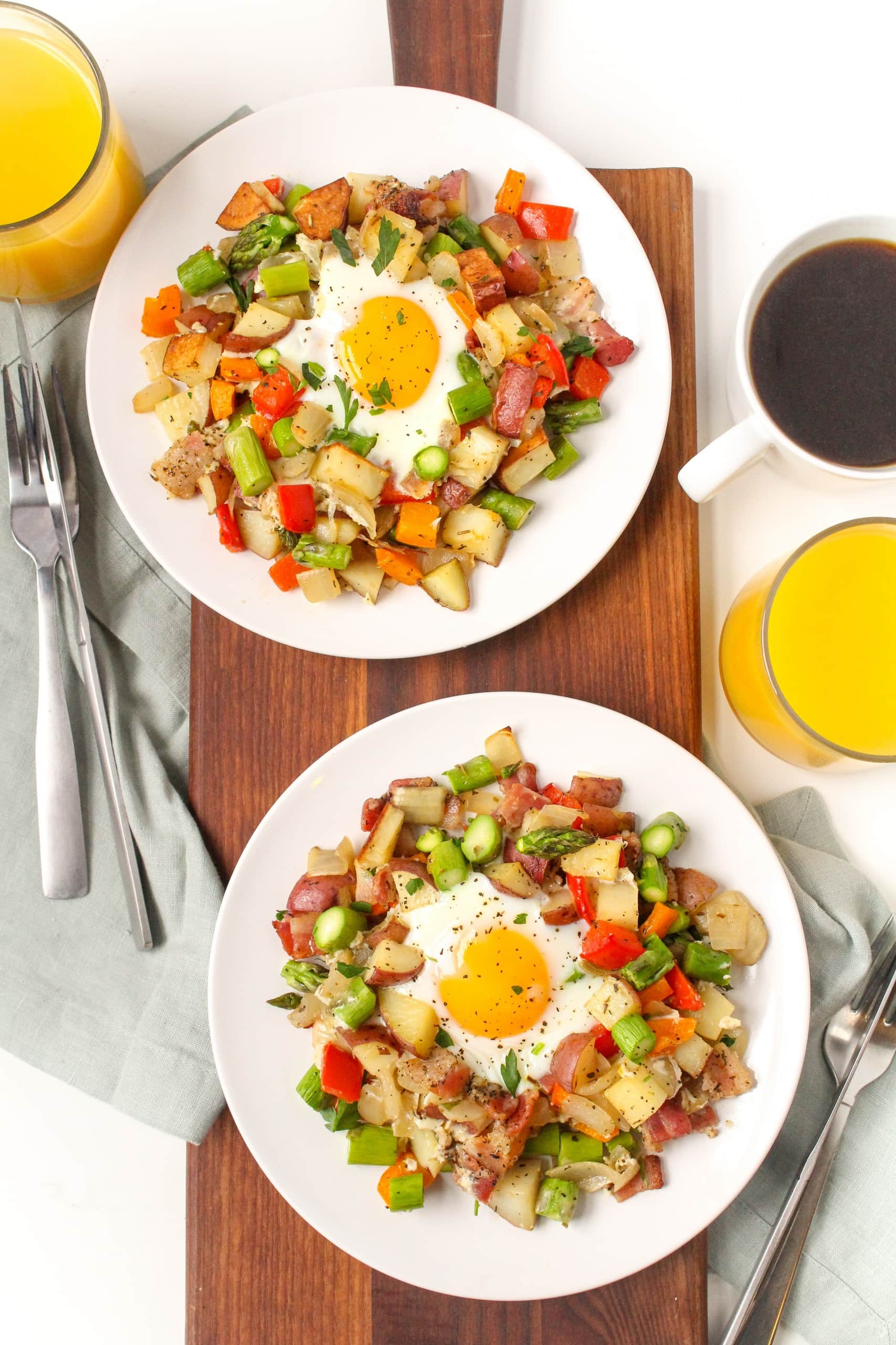 potato breakfast hash with baked eggs on two plates next to a mug of coffee and glass of orange juice