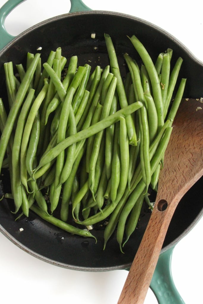 string beans in a skillet with a wooden spoon