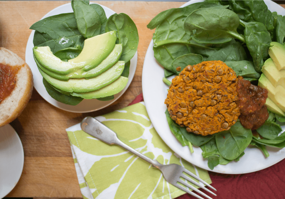lentil and chickpea patties on a bed of greens with sliced avocado