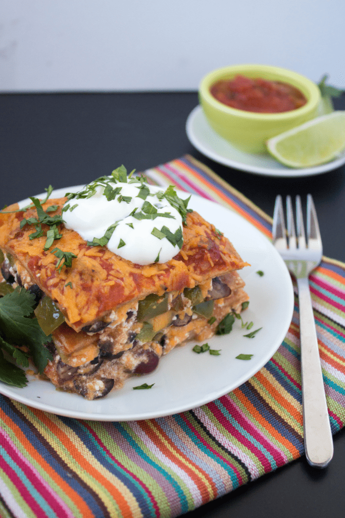 a slice of mexican lasagna casserole with a bowl of salsa