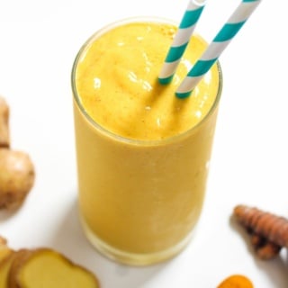 creamy mango turmeric smoothie with pineapple and ginger in a glass with striped straws