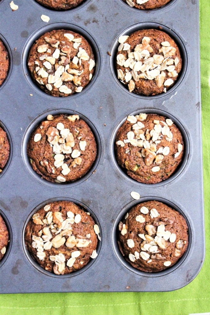 baked whole wheat muffins in a muffin tin with oats on top