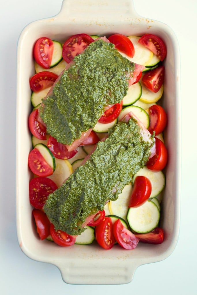 salmon filets with pesto sauce on top in a white baking dish with vegetables