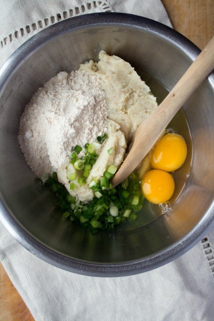 eggs, herbs, and mashed potatoes in a mixing bowl with a wooden spoon