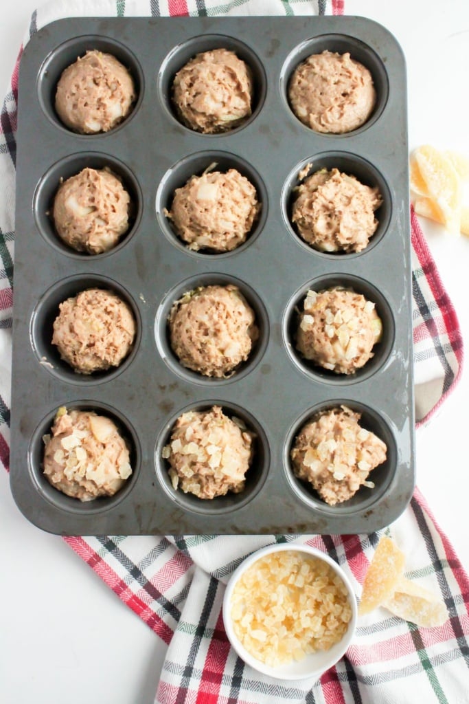 muffin batter in a muffin tin with diced candied ginger on top