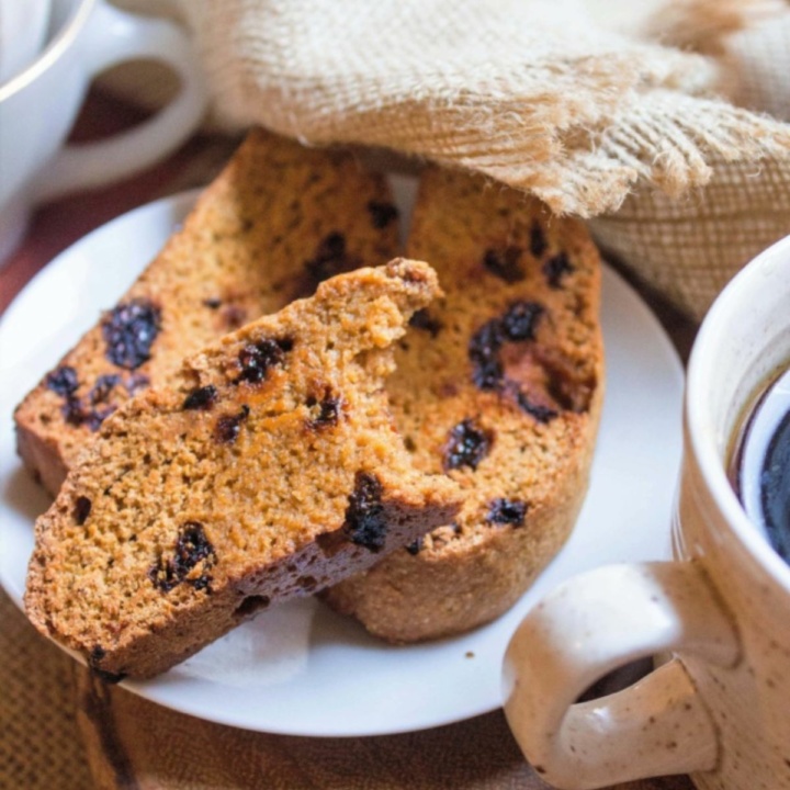 three spiced pumpkin biscotti cookies on a white plate beside a beige coffee mug