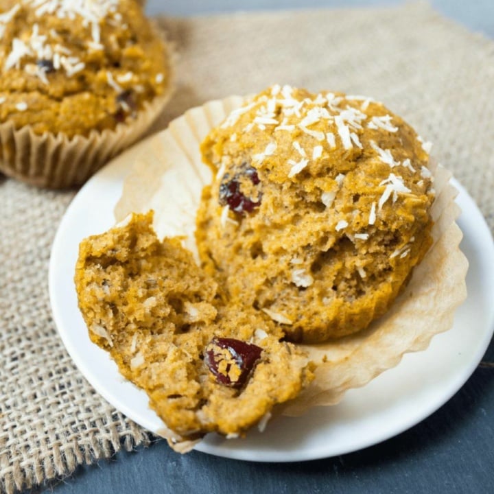 a sweet potato muffin with coconut and dried cranberries torn in half on a white plate