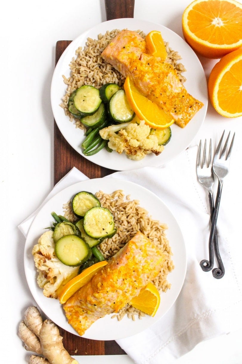orange ginger baked salmon on two plates with roasted zucchini and brown rice