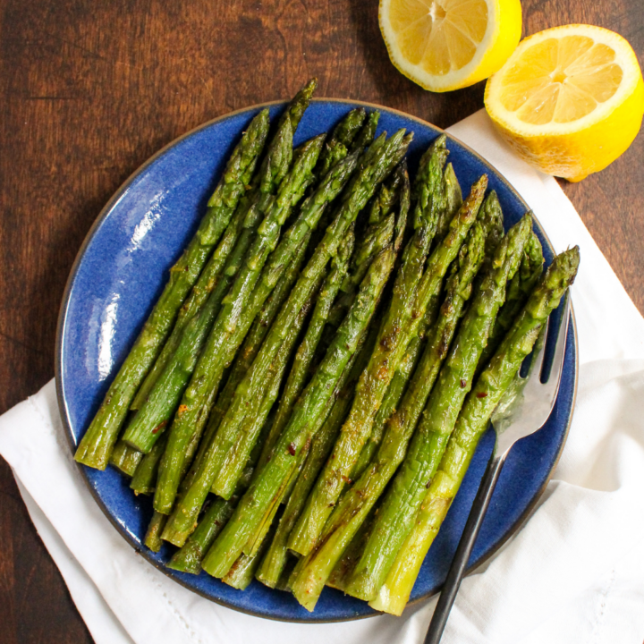 roasted asparagus on a white plate with lemons