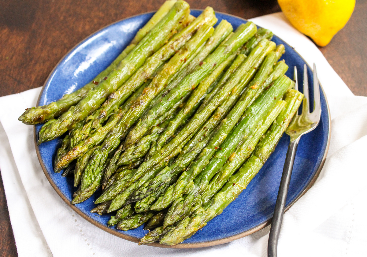 roasted asparagus on a white plate with lemons