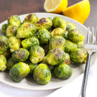 roasted brussels sprouts on a white plate with lemons