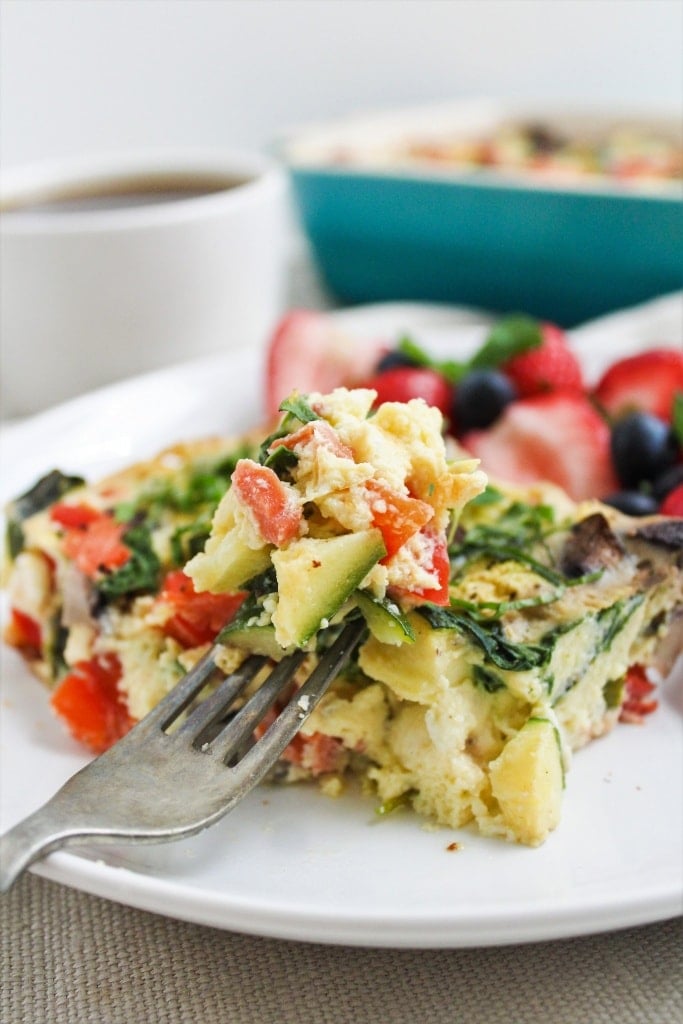 slice of veggie egg casserole with a spoonful on a fork and a coffee mug in the background