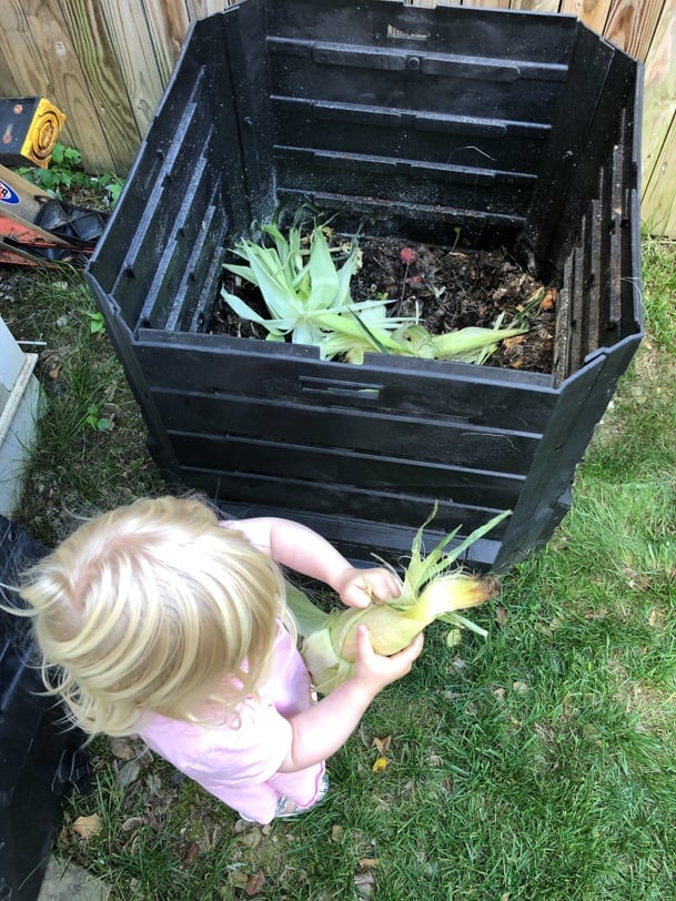 toddler shucking corn into a compost bin