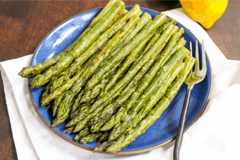 roasted asparagus on a white plate with lemons