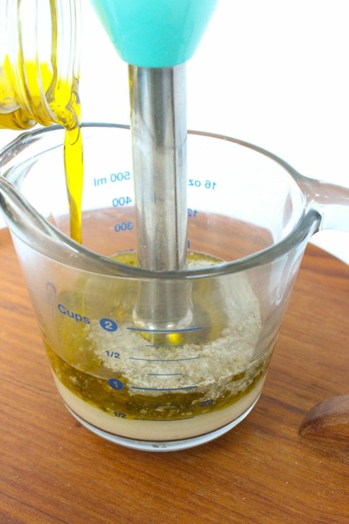 olive oil being streamed into a glass measuring cup with an immersion blender