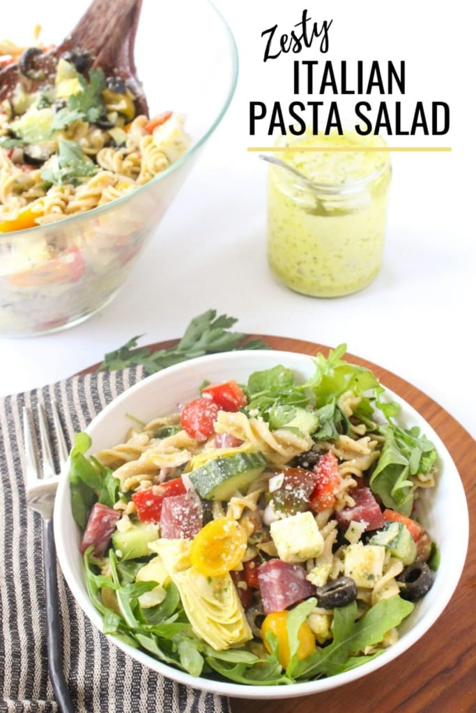 pasta salad with vegetables and cheese in a bowl next to a jar of Italian dressing