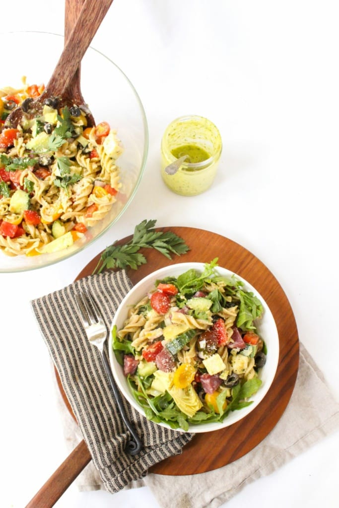 pasta salad in a bowl with arugula next to a jar of creamy Italian dressing