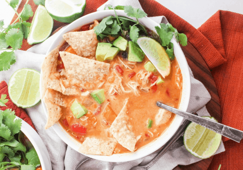 chicken tortilla soup topped with tortilla chips, avocado, lime, and cilantro