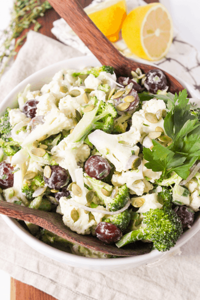 broccoli cauliflower salad in a large bowl with wooden salad spoons and sliced lemons