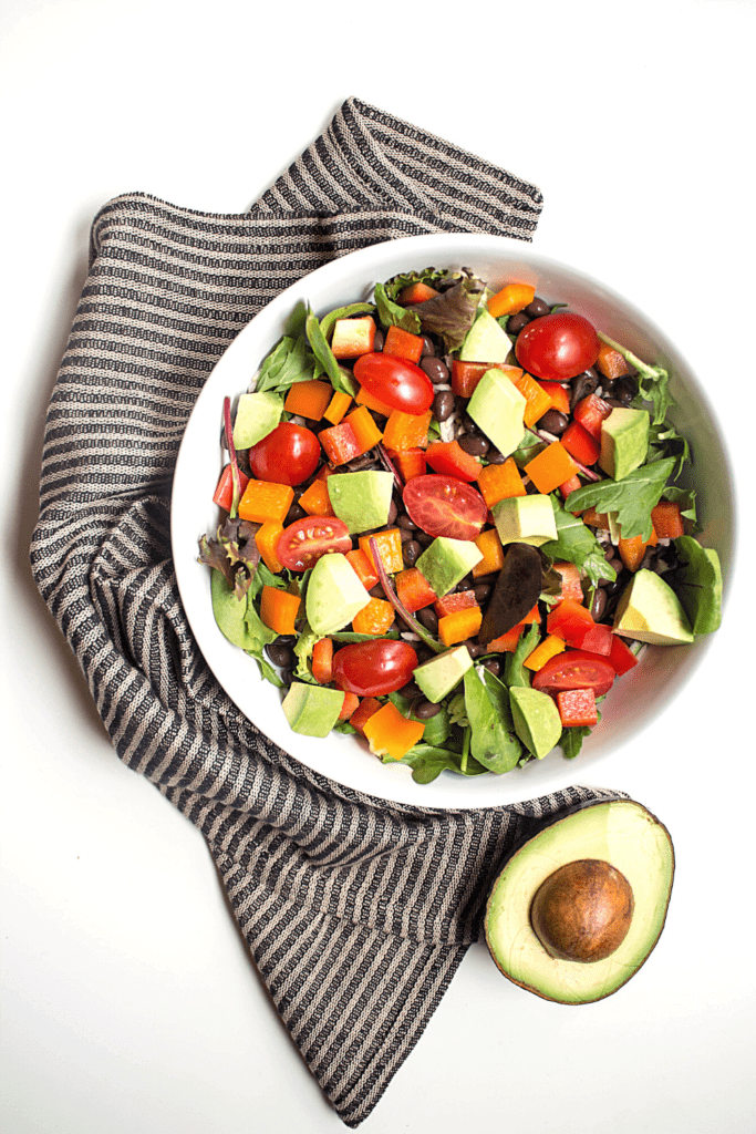 vegan mexican salad in a white bowl with a sliced avocado on the side