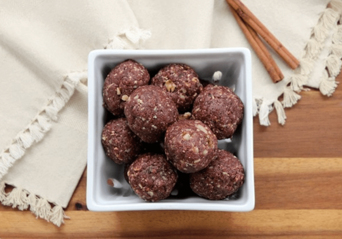 cherry almond snack bites in a square container with cinnamon sticks beside it