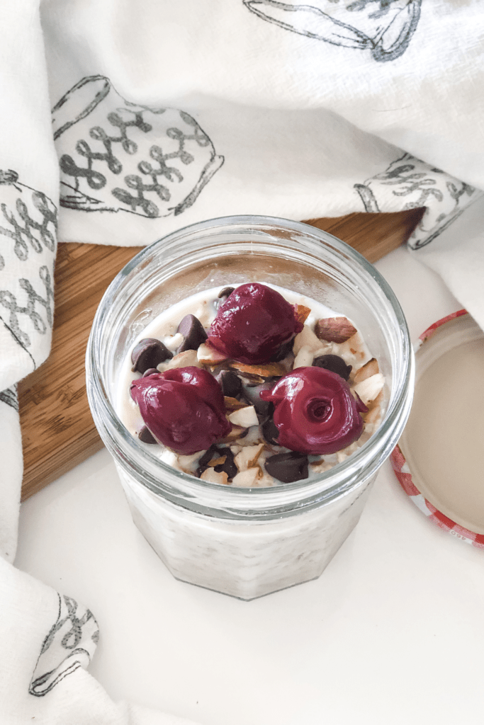 overnight oats with cherries, chocolate chips, and sliced almonds in a mason jar with a kitchen towel surrounding it 