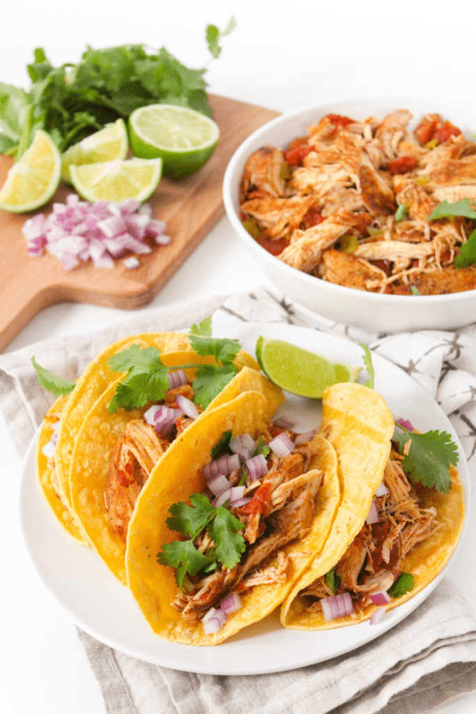 shredded chicken tacos with sliced limes and red onions in the background