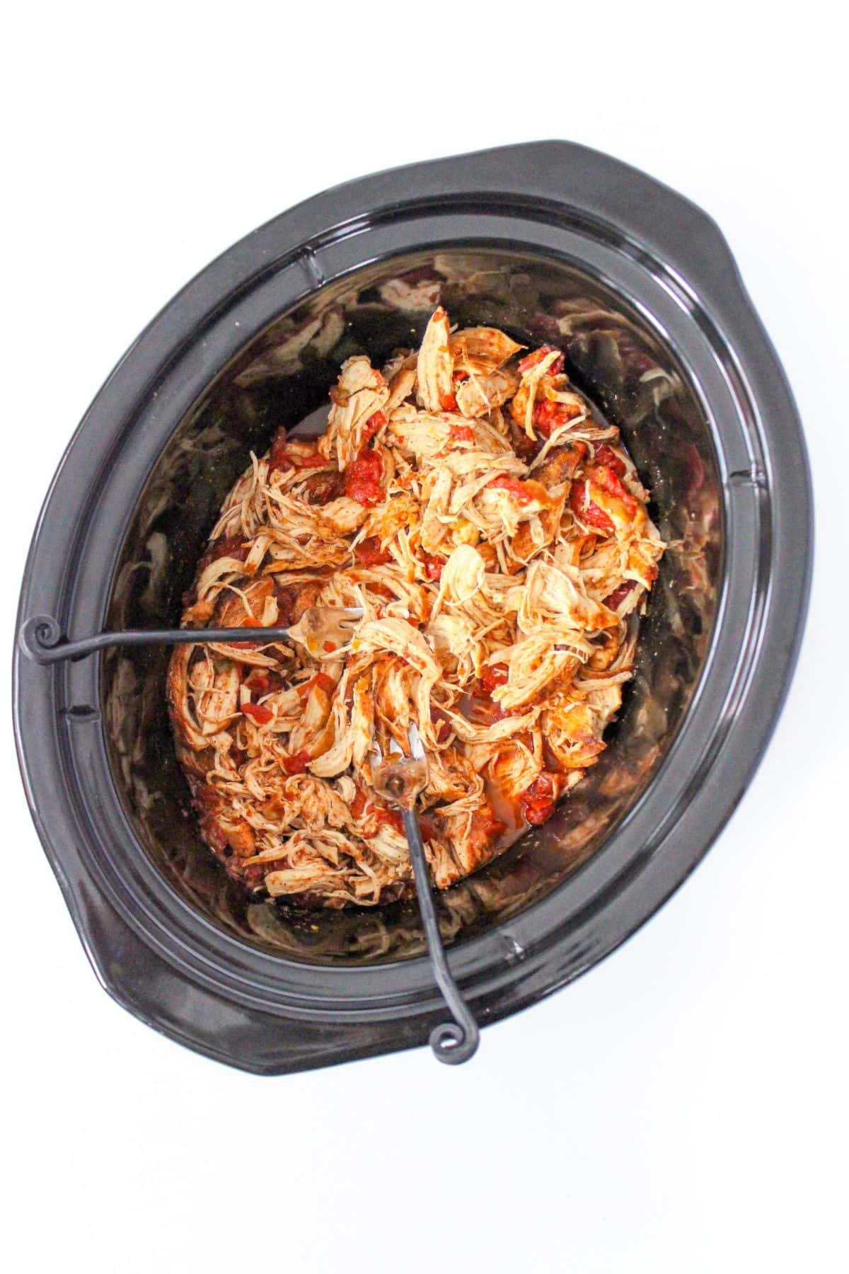 Mexican shredded chicken with diced tomatoes in a Crockpot insert with two forks