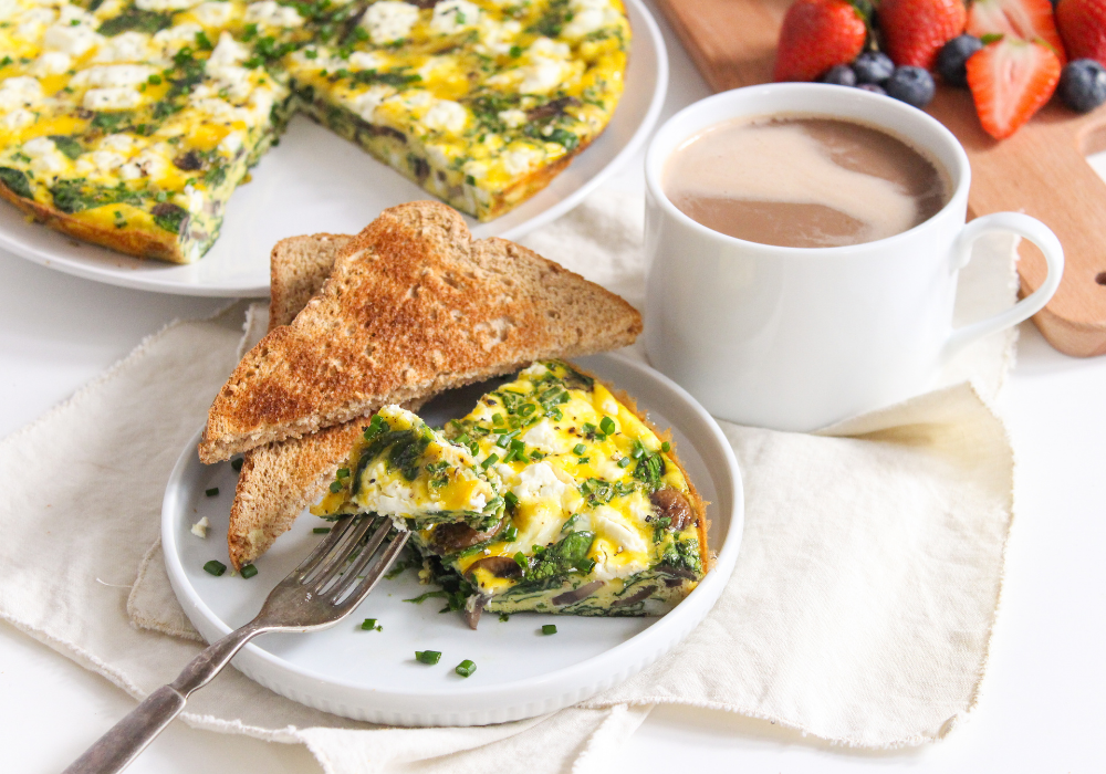 slice of goat cheese frittata on a white place with slices of toast and a coffee cup beside it