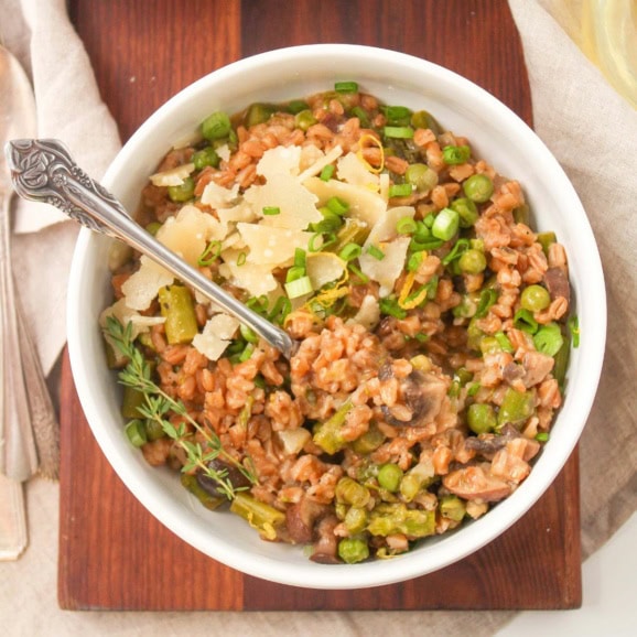 farro risotto in a bowl with mushrooms and asparagus topped with grated parmesan cheese